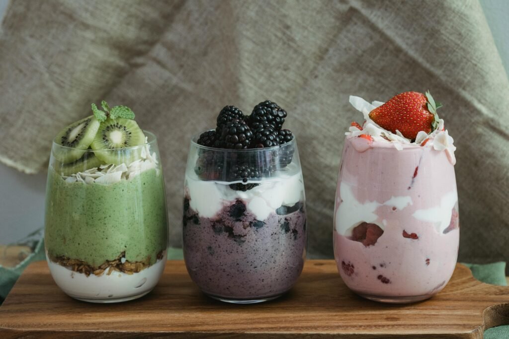 Delicious yogurt parfaits with kiwi, blackberries, and strawberries on a wooden board.